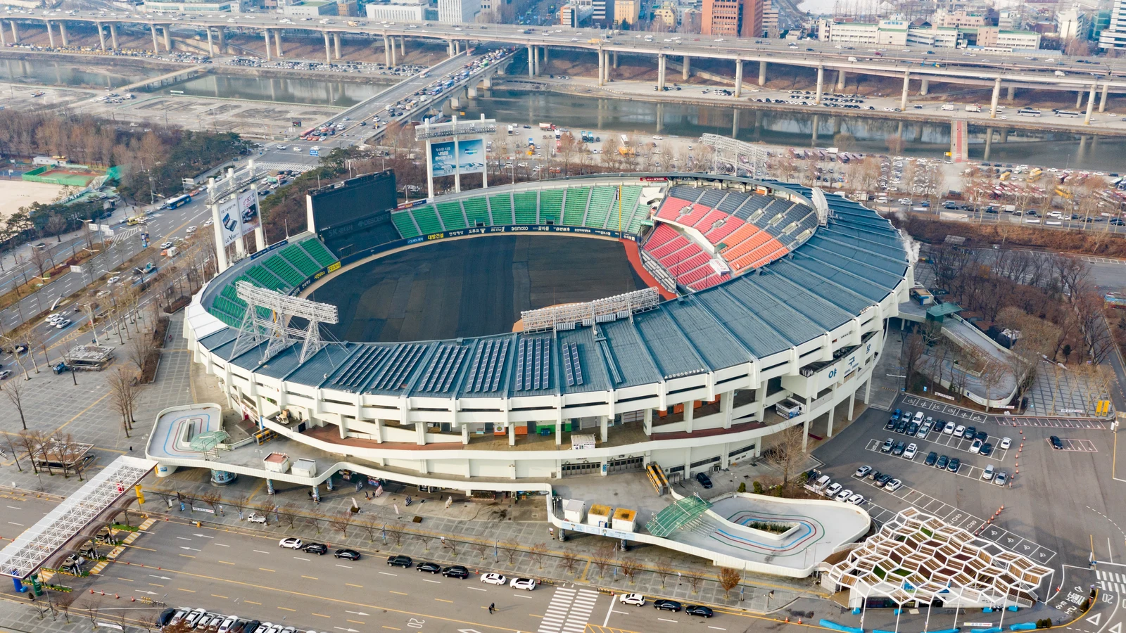 Jamsil Baseball Stadium from above in winter, its field under covers, with the Han River and its bridges behind