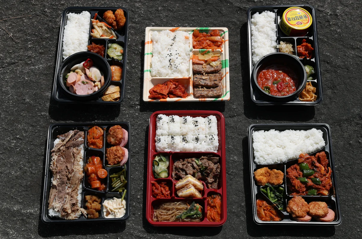 A top-down spread of Korean convenience-store dosirak (lunchboxes) — rice, a protein, and several banchan packed into each tray