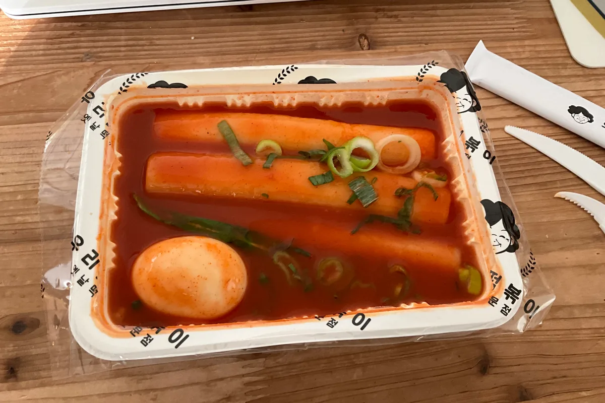 A pan of tteokbokki — chewy rice cakes and fish cake in glossy red gochujang sauce